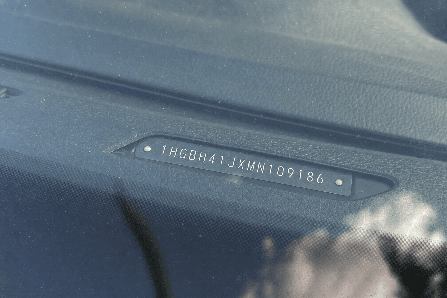 Close-up of a car's metal VIN plate on the dashboard seen through the windshield glass
