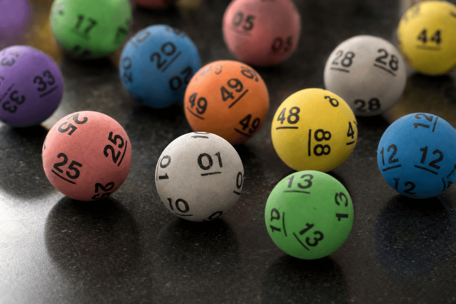 A scatter of colorful numbered lottery balls on a dark reflective surface