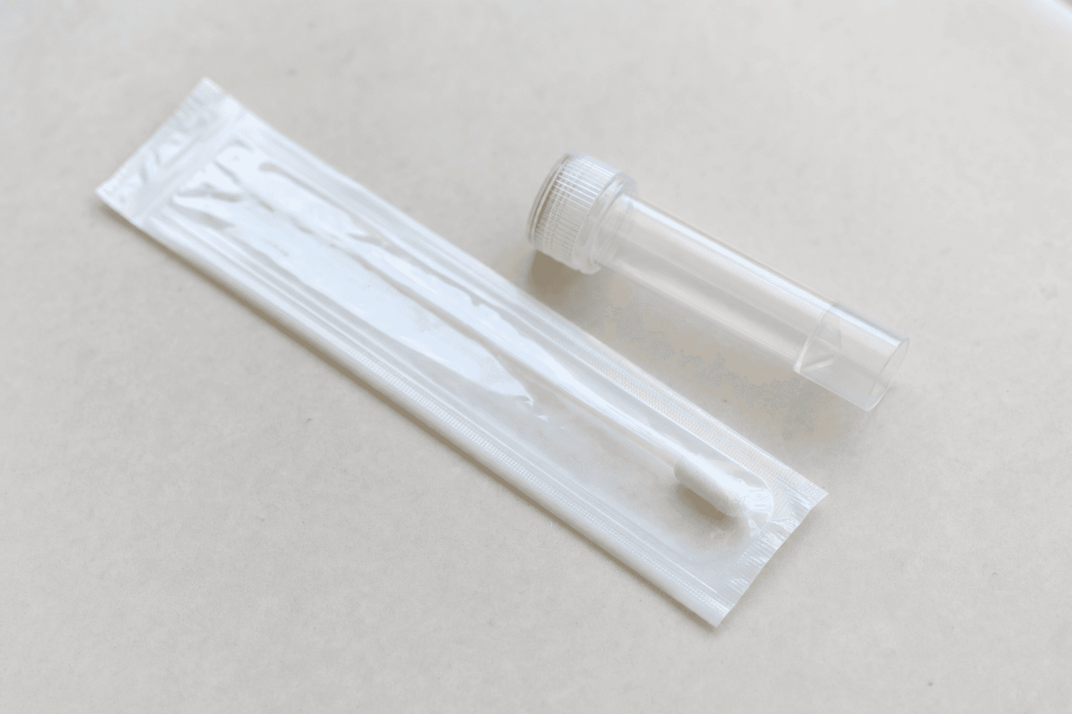 A genetic test kit with a sealed cheek swab and a small specimen tube on a light table