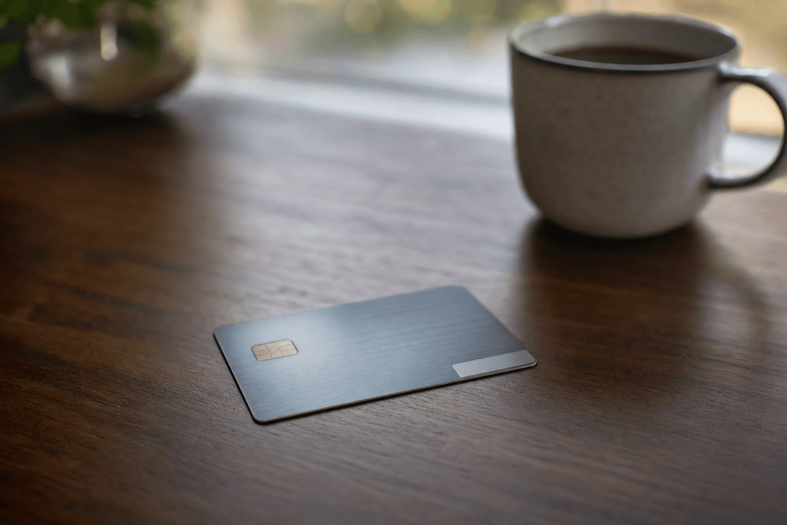 A single credit card resting on a dark wood desk in warm morning light, a coffee mug softly out of focus behind it