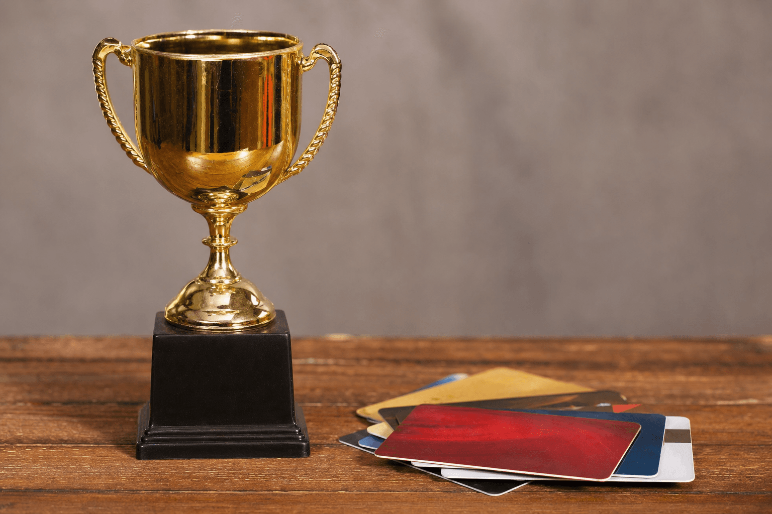 A shiny gold trophy on a wooden table beside a fanned-out stack of assorted gift cards