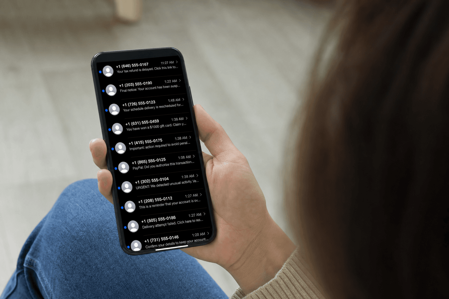Person holding a phone showing a crowded text message inbox full of scam alerts, delivery notices, and fake fraud warnings